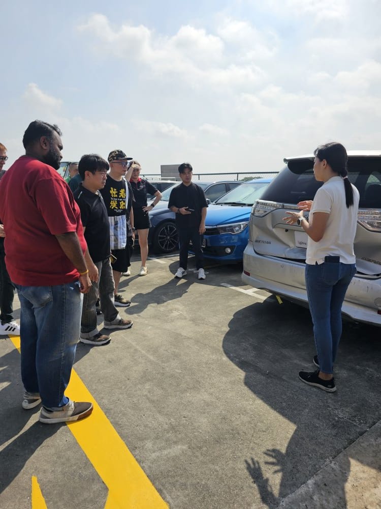 Igive assessor explaining hidden vehicle damage to a group around a car