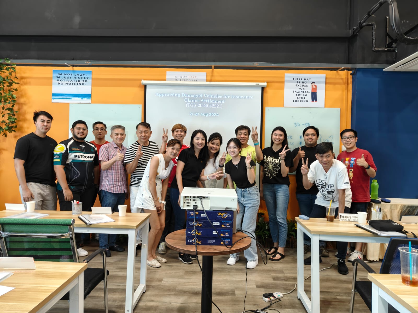 A graduating Igive training cohort posing with their trainer in front of a classroom whiteboard.